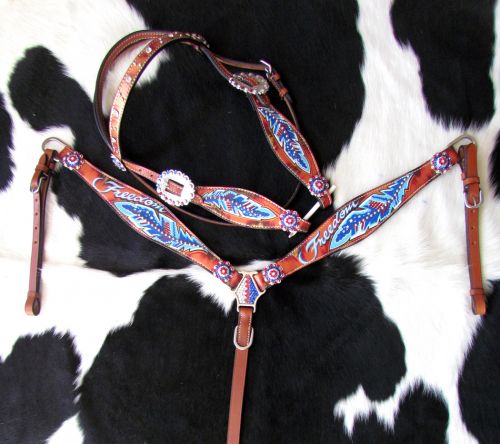 Medium oil headstall set with painted red, white, and blue feather and the word "Freedom" with red, white, and blue conchos accenting the piece. Headstall set lays on a black and white cowhide rug. 