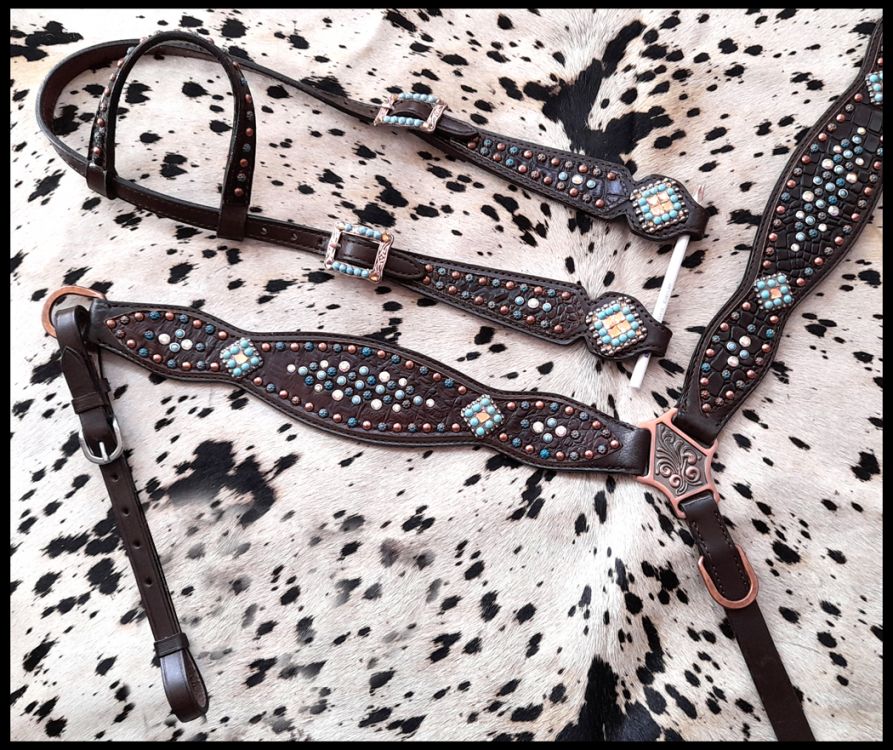 Dark oil western headstall set with gator print leather. Teal, copper, and white studs accent the set with turquoise and silver conchos. Black and white cowhide rug. 