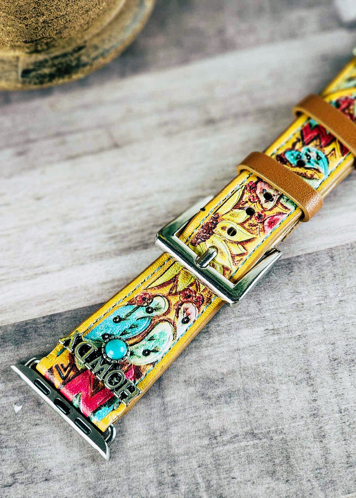 Yellow apple watch band with floral tooling painted. Watch band has silver accent reading "Howdy" with a turquoise colored stone. Close up shows the buckle. 
