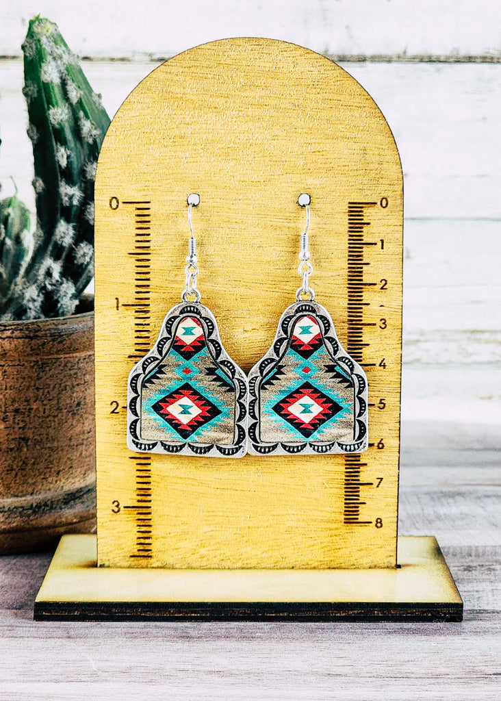 Southwestern cow tag leather earring with stamped designs. Teal, red, and white tribal design. Measuring about 2.5".