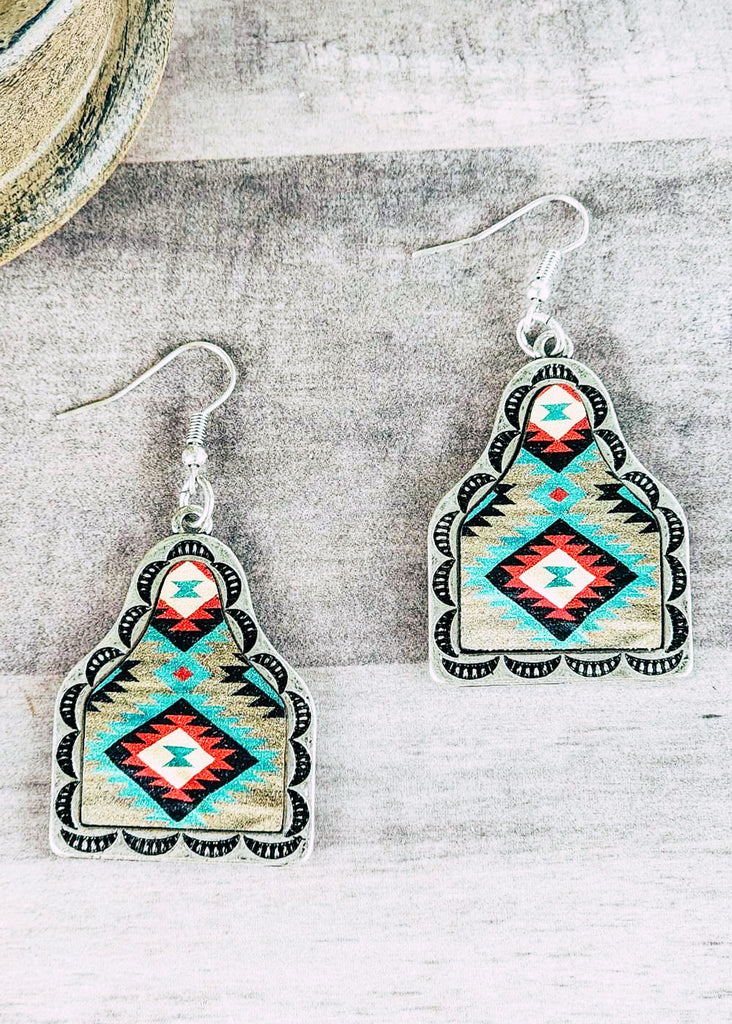Southwestern cow tag leather earring with stamped designs. Teal, red, and white tribal design. 