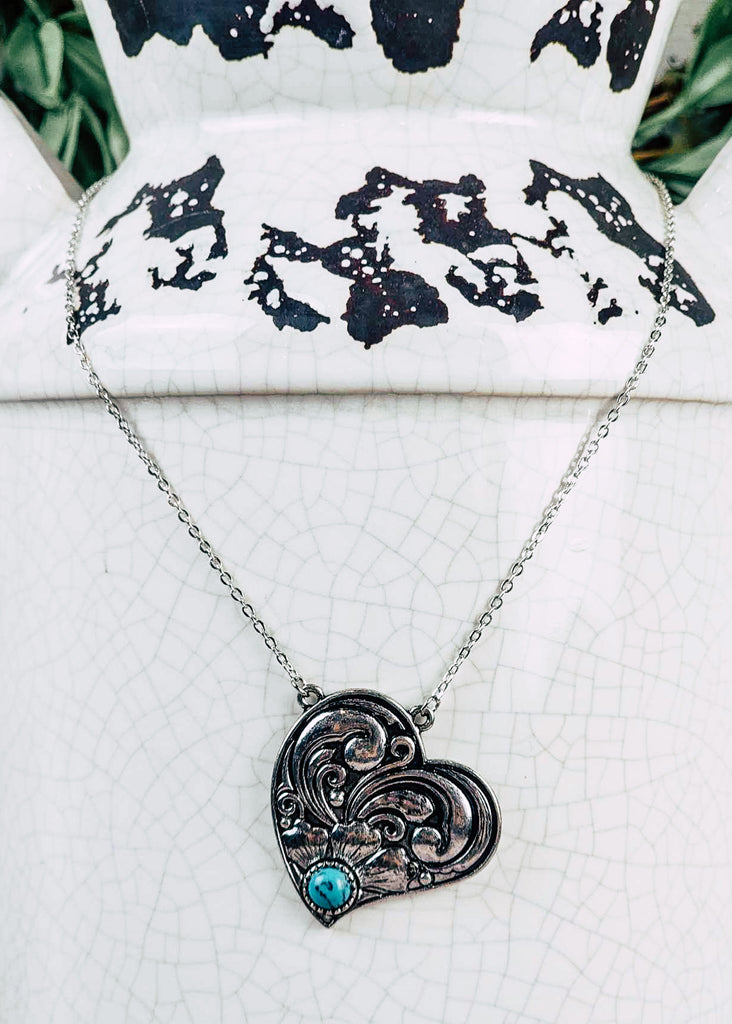 Western cowgirl heart antique silver floral design and a turquoise-like stone acting as the middle of flower. Chain necklace with clasp. 