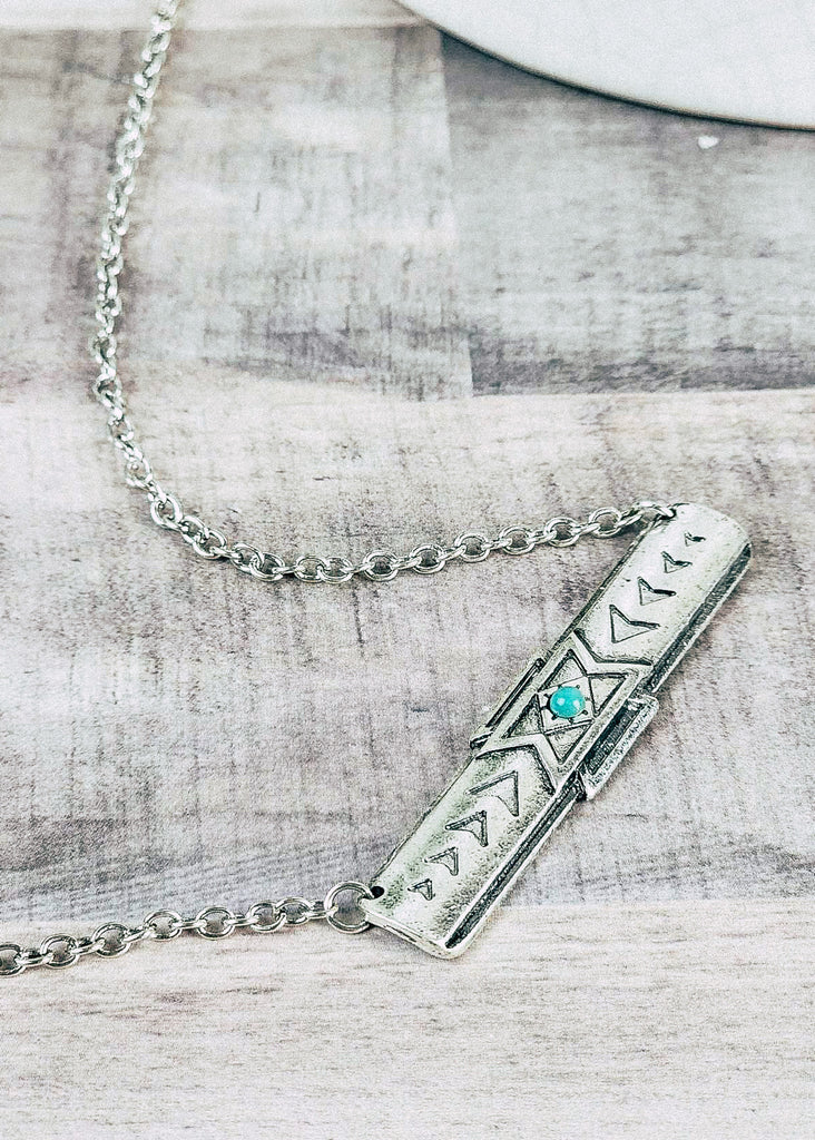 Southwestern cowgirl necklace with a tribal bar necklace pendant with a turquoise-like stone in the middle. Chain holding the necklace. 