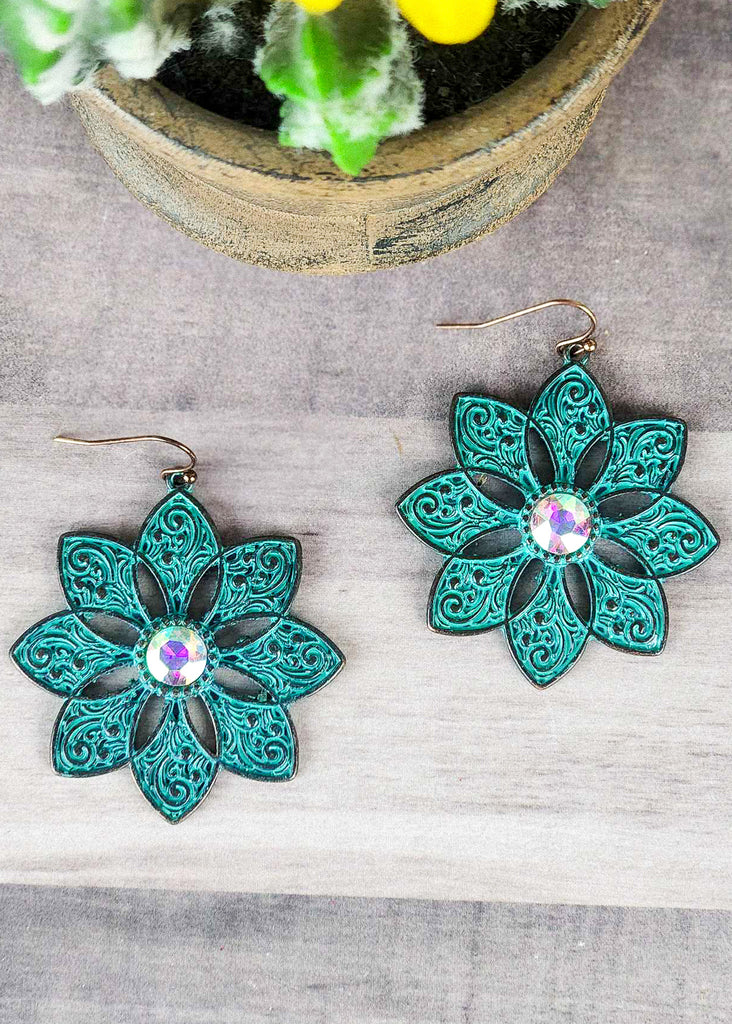 Cowgirl antique silver with teal inlay floral earrings with jewel stone that changes color in different lighting. Laying on wooden table. 
