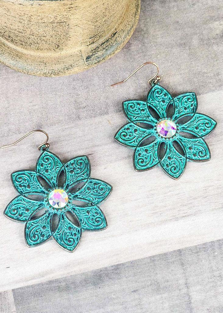 Cowgirl antique silver with teal inlay floral earrings with jewel stone that changes color in different lighting. Laying on a wooden table. 