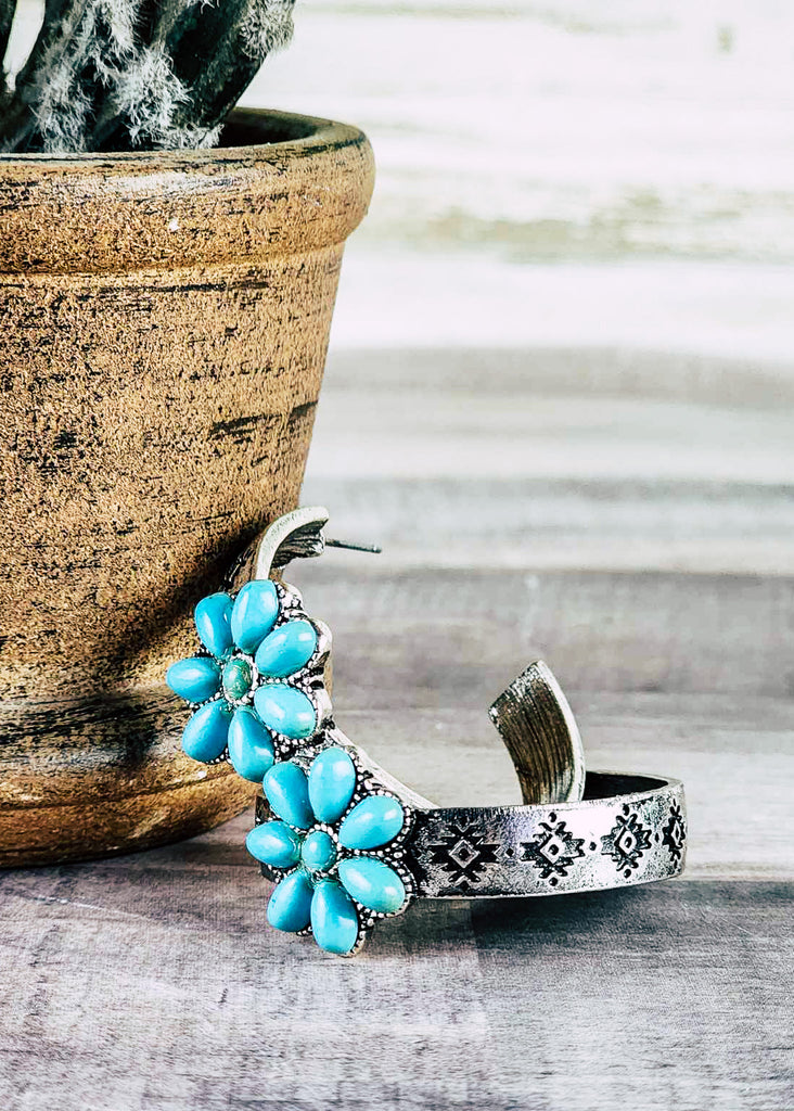 Cowgirl hoop stud earring with floral turquoise like stone design. Antique silver stamped hoops. Laying next to pot on wood  counter. 