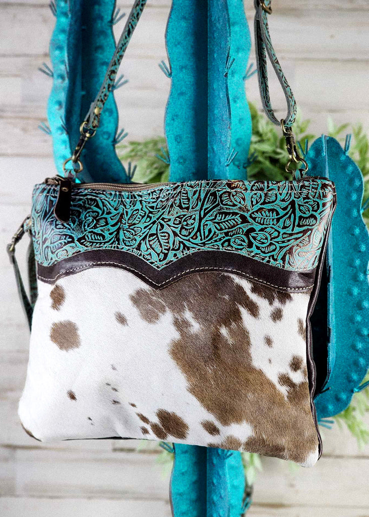 Hanging &  Angled. Tooled leather accent with cowhide shown to side seam. Wristet visible. Matching tooled leather shoulder strap visible. 