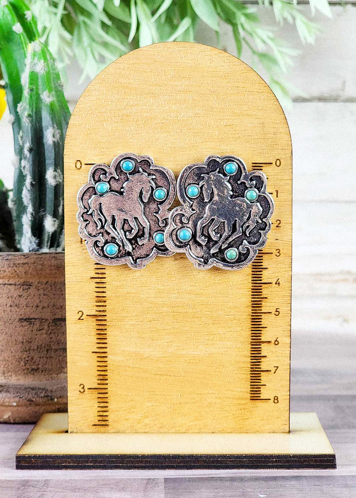 Cowgirl earrings with a running horse engraved in the metal and turquoise like stones set around the horse.