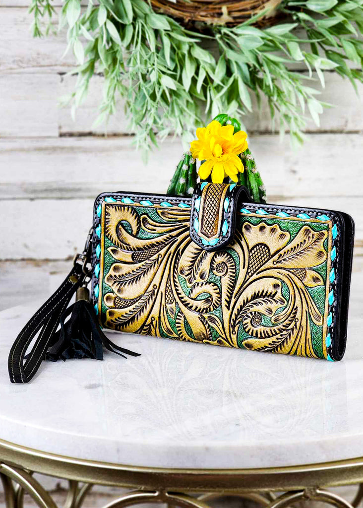 Cowgirl turquoise tooled wallet with turquoise bucksitch leaning against a cactus.