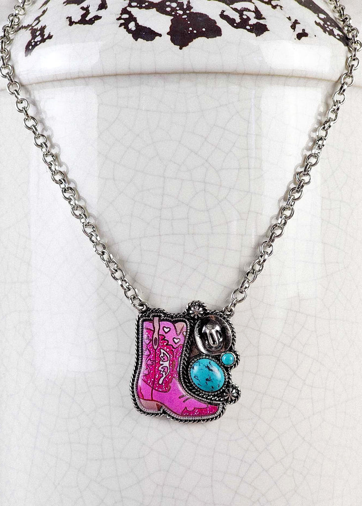 Cowgirl necklace with bright pink epoxy boot design with two turquoise like stones and antique silver designs including a cowboy hat and conchos. 