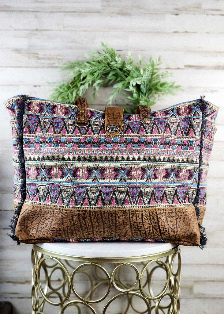 Southwestern weekender bag with hues of purple tribal design. Leather paneling on the bottom and matching leather handle and snap clip. 