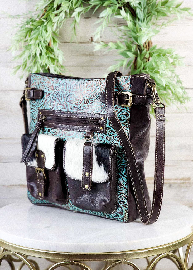 Angled view. Turquoise tooled leather meeting a dark brown leather on the back side. Adjustable straps shown. 