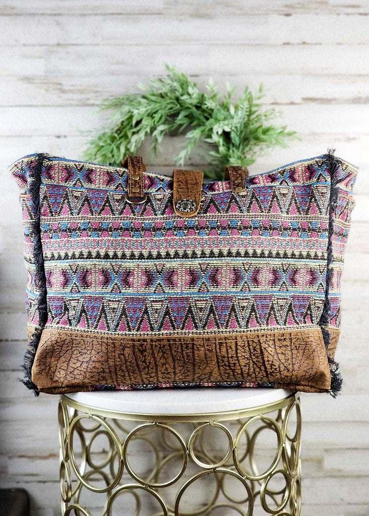 Southwestern weekender bag with hues of purple tribal design. Leather paneling on the bottom and matching leather handle and snap clip. 