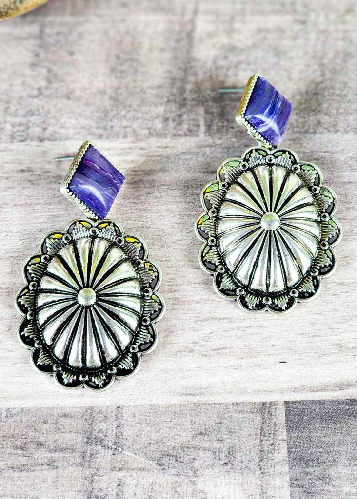 Purple stone set in antique silver while antique silver concho sets on wooden table. 