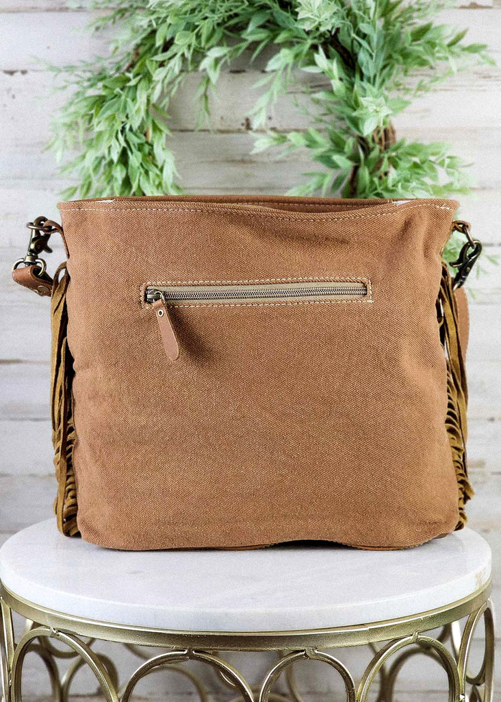 Back of purse sitting on marble stool. Brown canvas material with side zipper showing. 