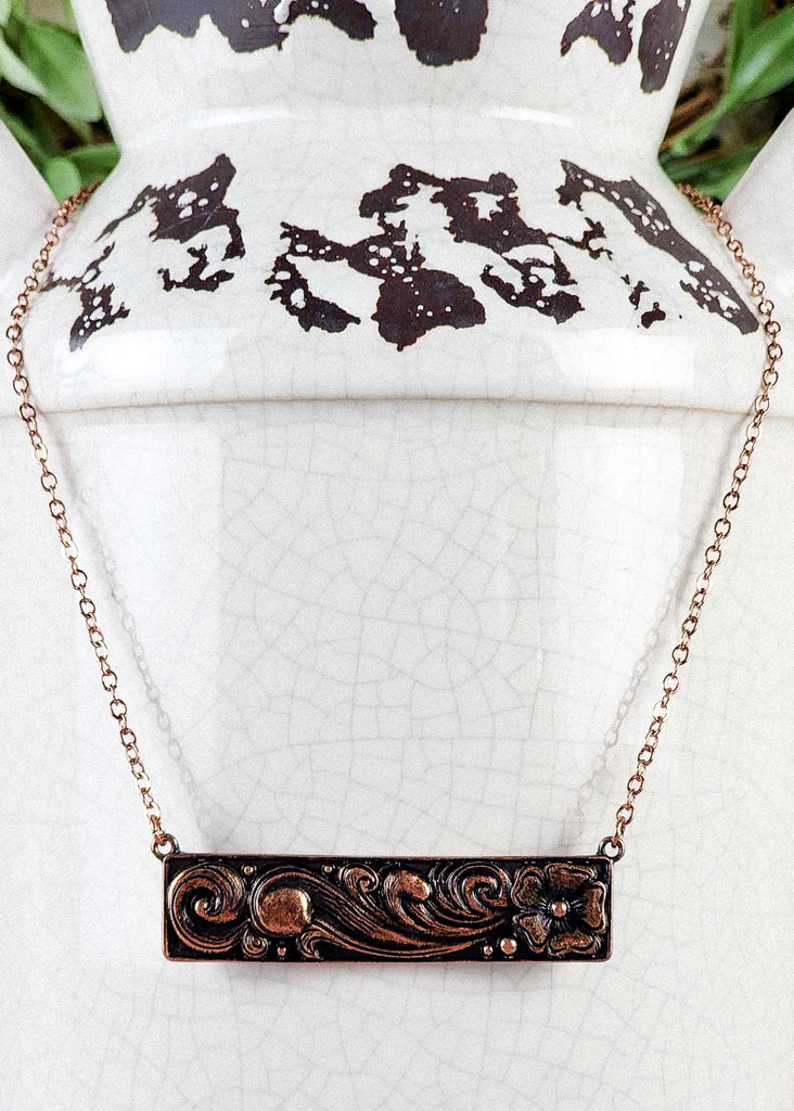 Cowgirl floral metal tooling bar necklace with copper coating. Bar necklace is connected to a copper chain. 