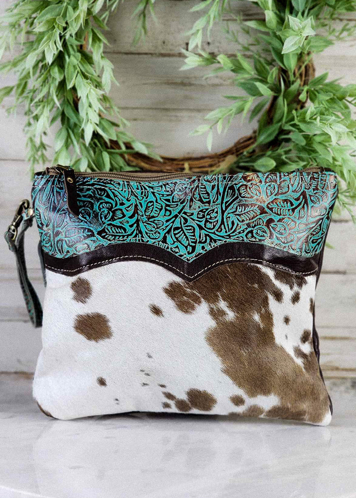 Front View. Western handbag with tooled leather teal accents and cowhide. Tooled leather wristlet. Shoulder straps have been removed. 