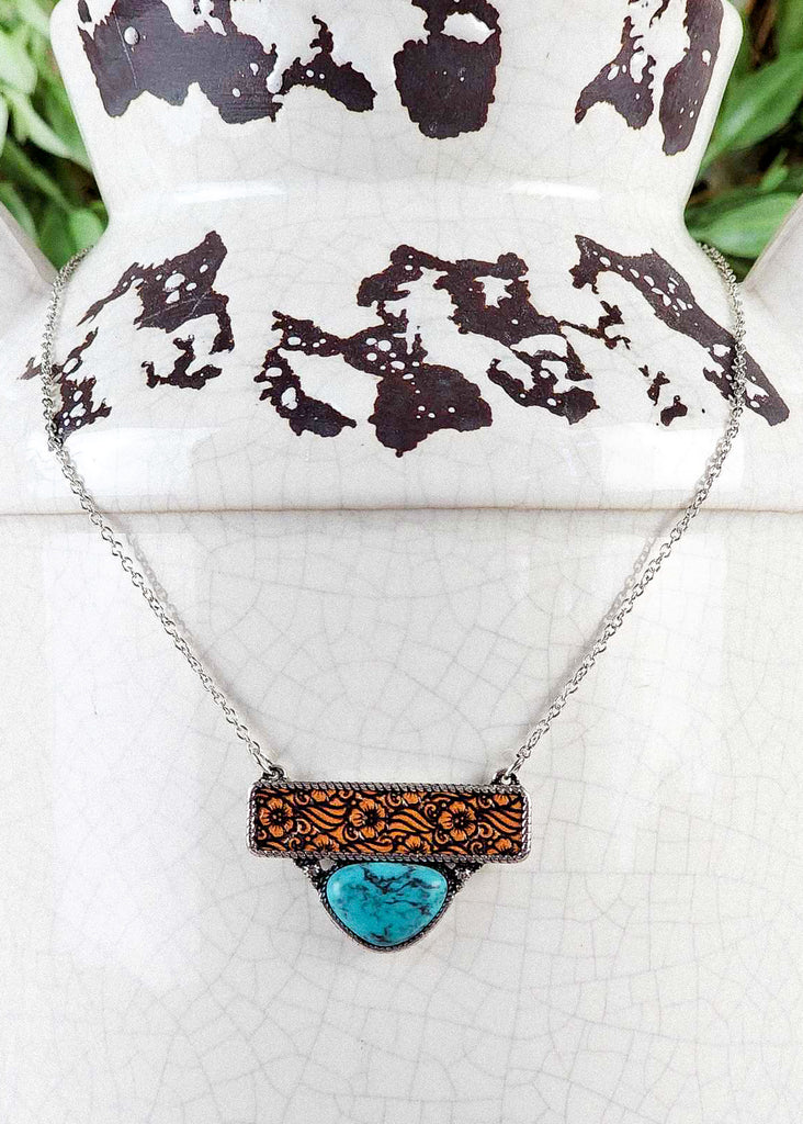 Cowgirl necklace with leather floral tooling and a turquoise like stone encased in a antique twisted silver design.
