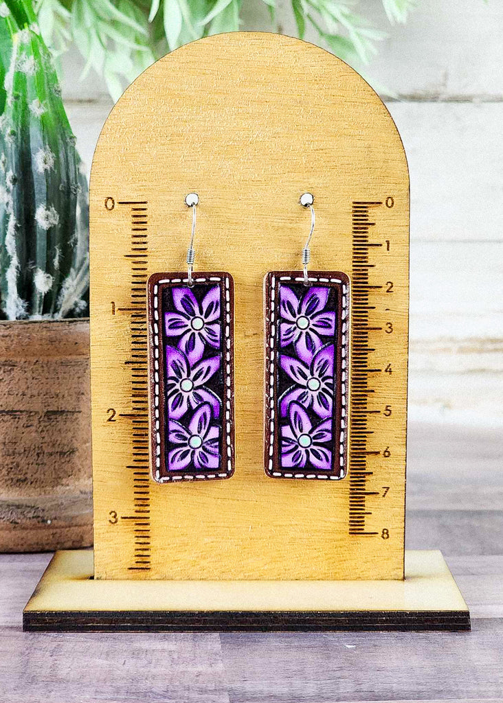Western leather tooled earrings with floral design. Painted purple with white painted stitching. 