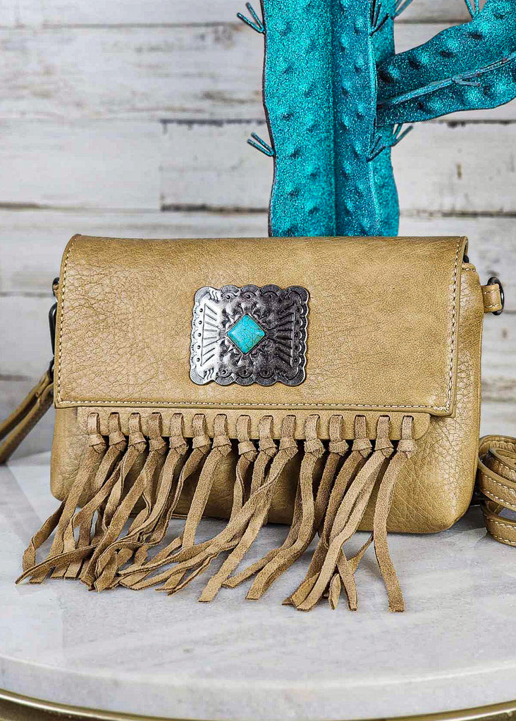 Tan western clutch with turquoise stone concho. Flap has hand tied fringe. Crossbody strap lies beside purse (almost off picture) and wristlet lays behind purse. 