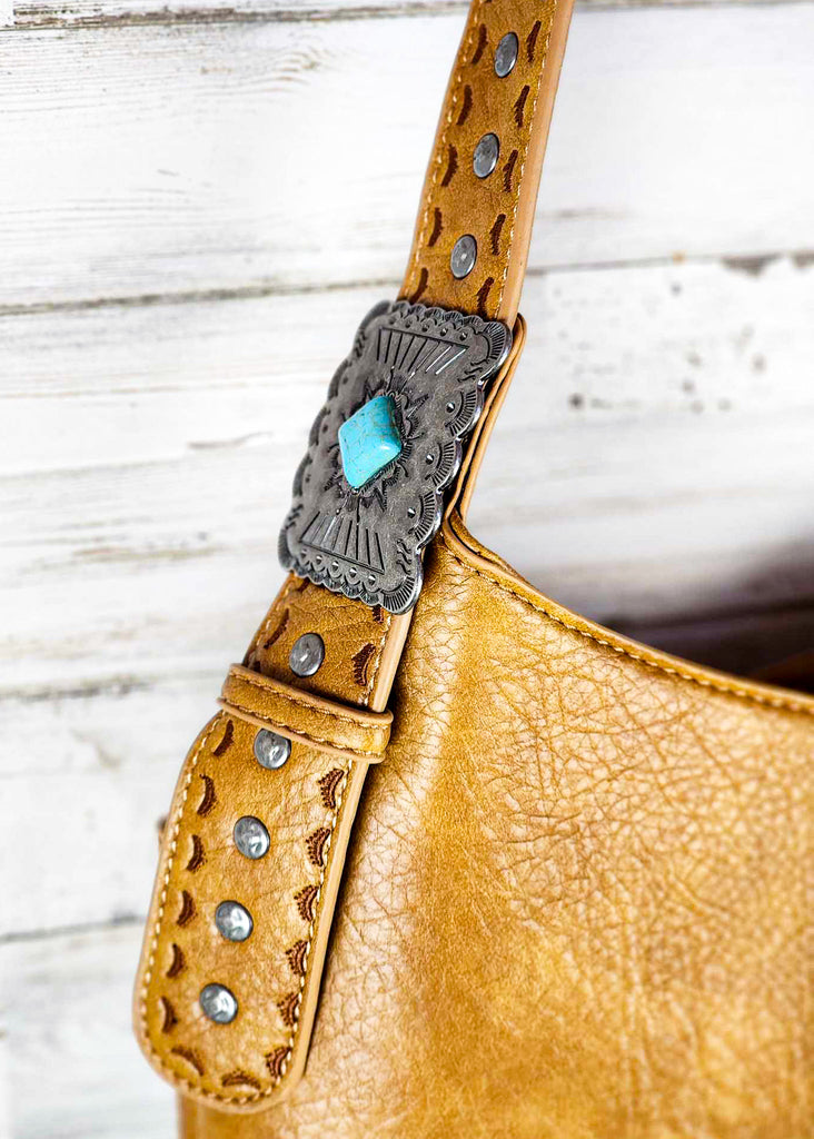 Brown wrangle hobo with adjustable shoulder strap with turquoise concho. Silver studs around concho on strap. 