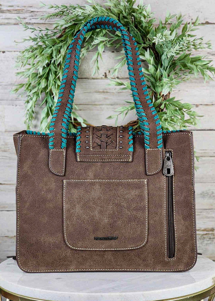 Backside of tote bag with open pocket and concealed carry zippered pocket. Turquoise whipstitch runs up handle of tote bag and on snap cross. 