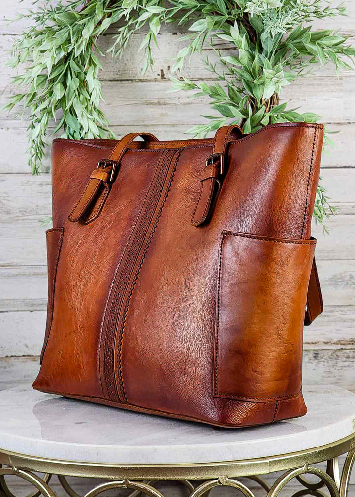 Western genuine brown leather with side pockets and beautiful stitch ribbon design down front. Copper buckles on tote handles.