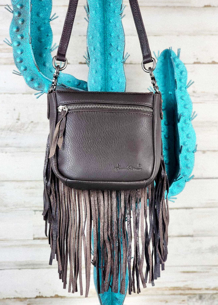 Backside of purse with zippered pocket visible. Fringe hangs from purse and adjustable and removable shoulder straps are visible.