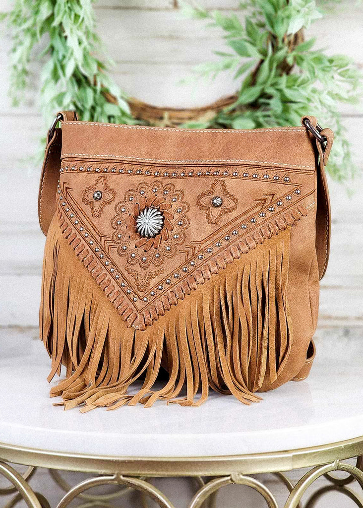 Western concealed carry fringe bag with antique silver concho and floral rough out. Matching leather fringe and adjustable shoulder straps. Bag sits on marble stool.