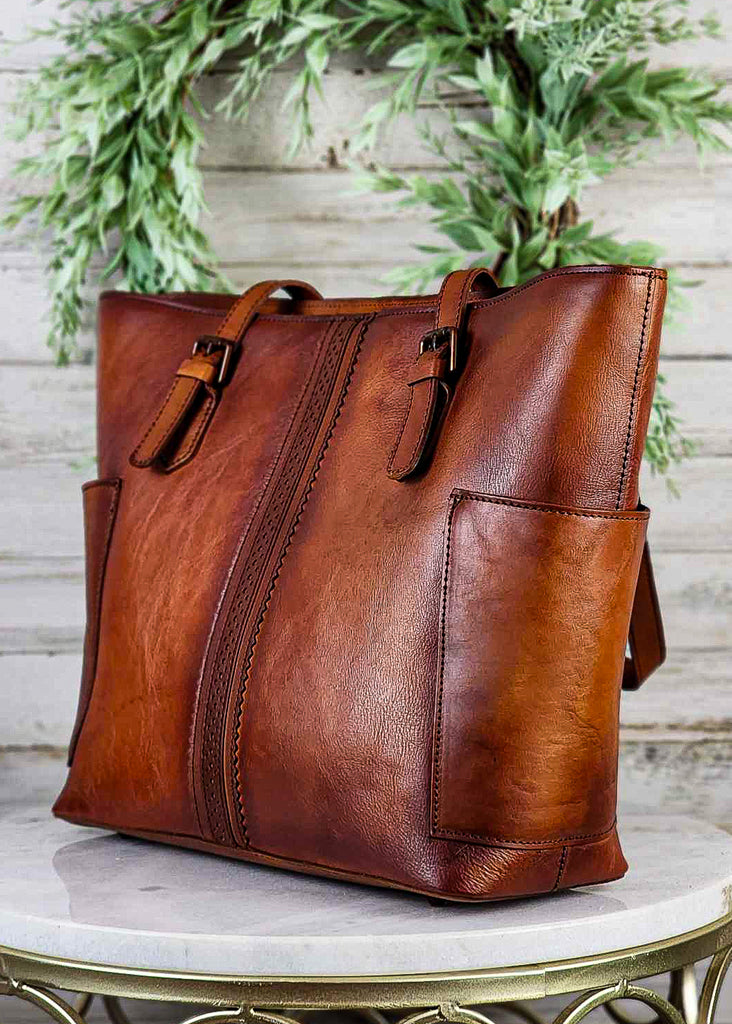 Western genuine brown leather with side pockets and beautiful stitch ribbon design down front. Copper buckles on tote handles.