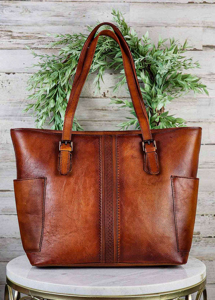 Western genuine brown leather with side pockets and beautiful stitch ribbon design down front. Copper buckles on tote handles.