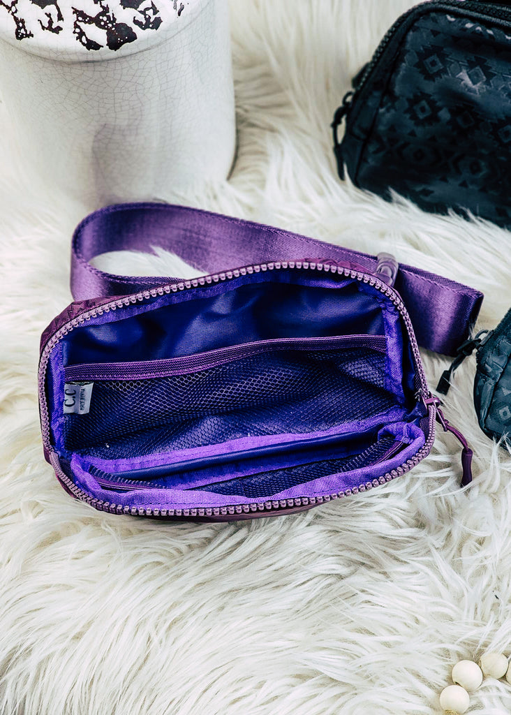 Purple Aztec embossed fanny pack. Adjustable waist strap seen, opened interior show netting storage. 