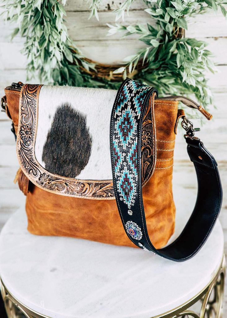 Western black & turquoise aztec guitar or purse strap with diamond like jewels throughout the strap. Silver concho with blue, purple, and red jewels. Shown attached to a brown leather purse with tooled and cowhide flap. 