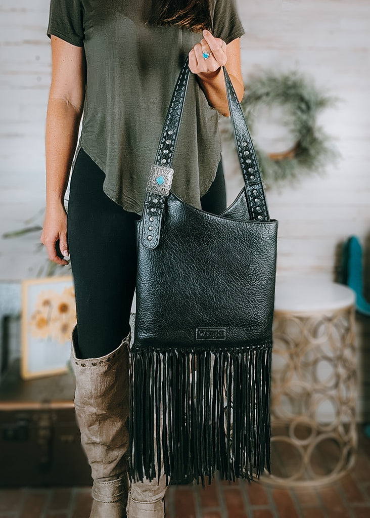 Concealed Carry Black Turquoise Stone Concho Fringe Hobo on model with olive green shirt, black leggings and tan knee high boots with western decor in the background