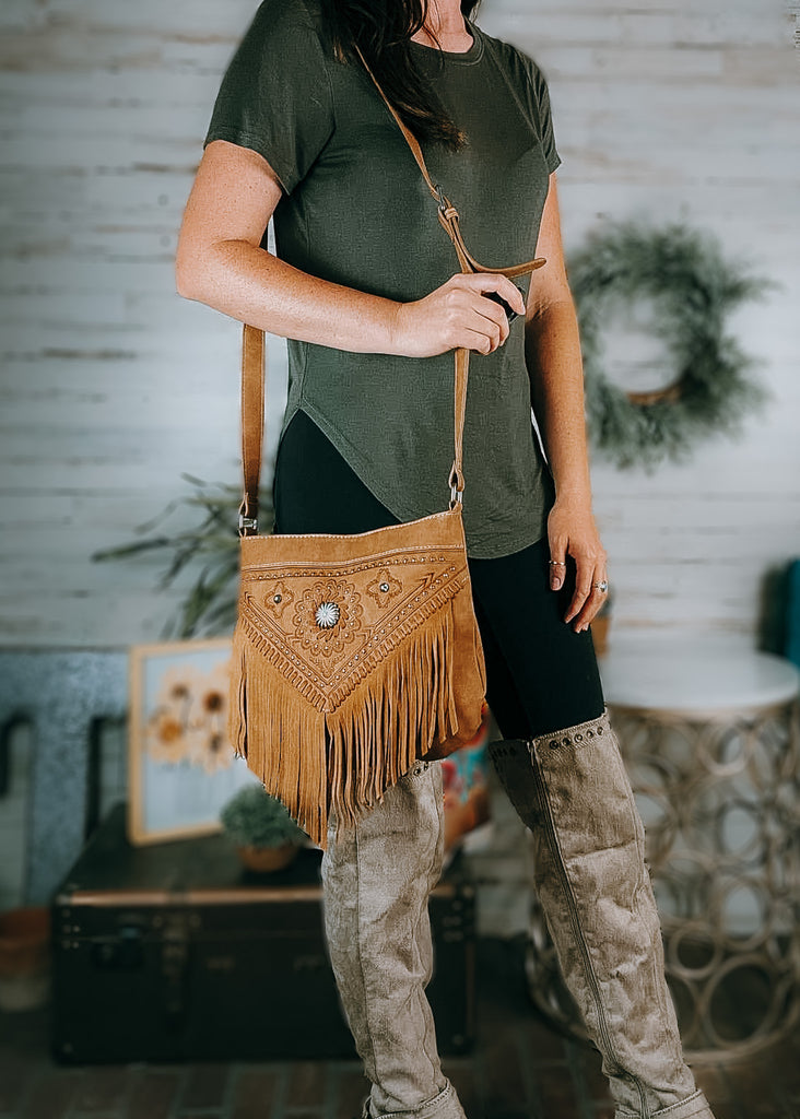Concealed Carry Concho Floral Fringe Crossbody Bag on model with olive green shirt, black leggings and tan knee high boots, western and farmhouse decor in the background