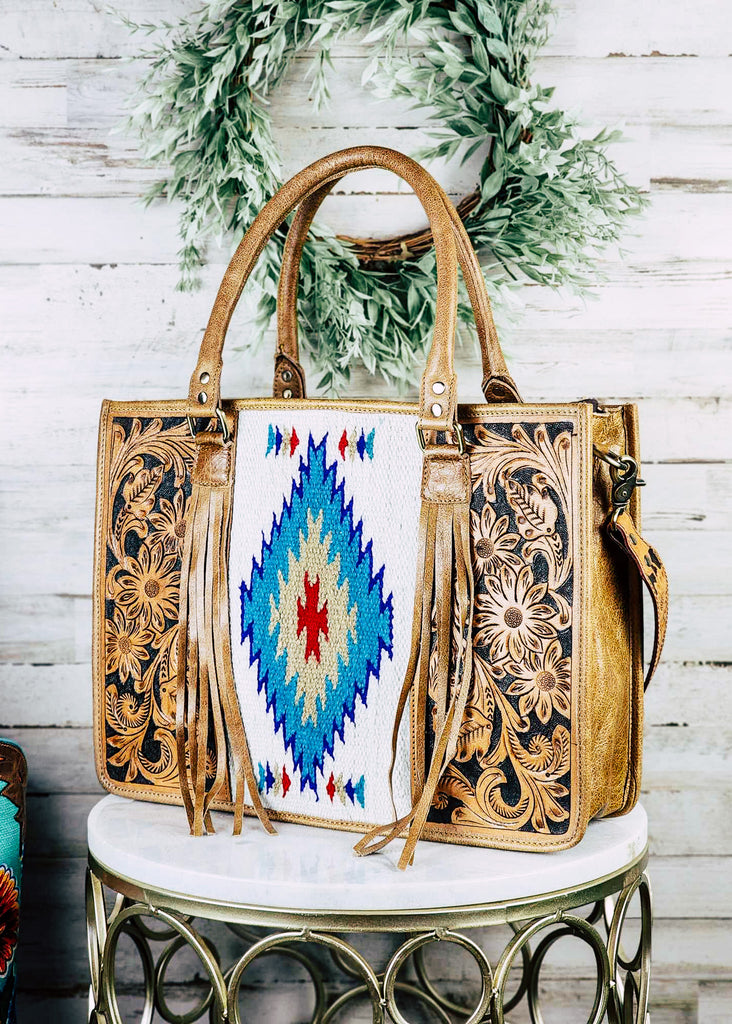 concealed carry western handbag with aztec pattern and tooled floral and fringe, shown on white table with green decor