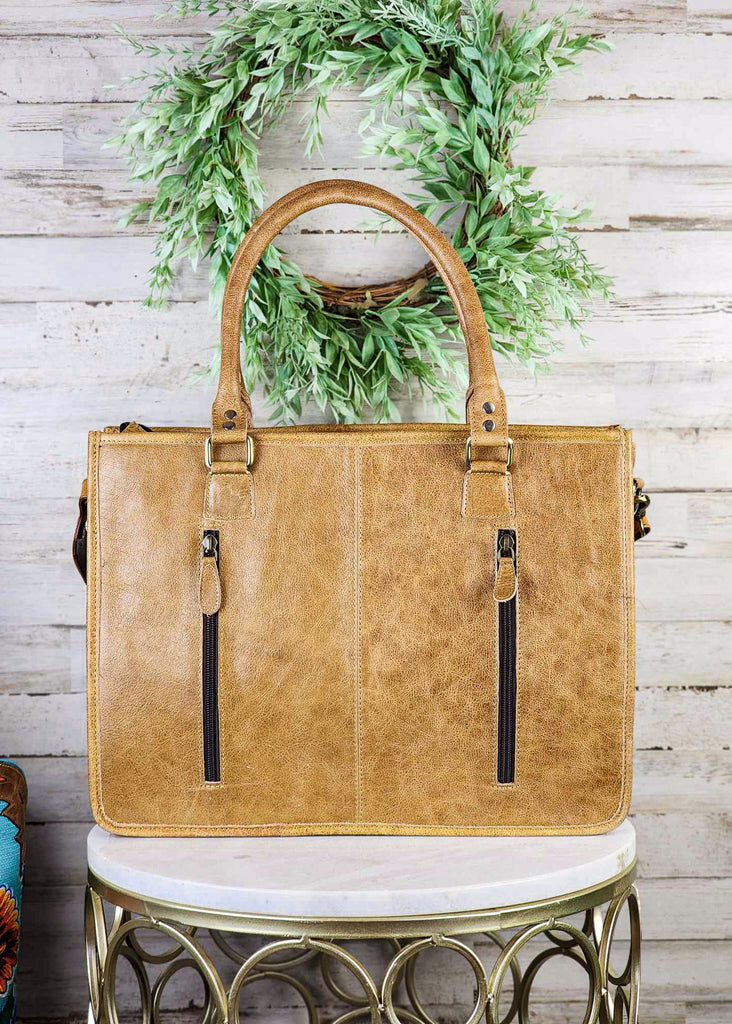 concealed carry western handbag with aztec pattern and tooled floral and fringe, shown on white table with green decor