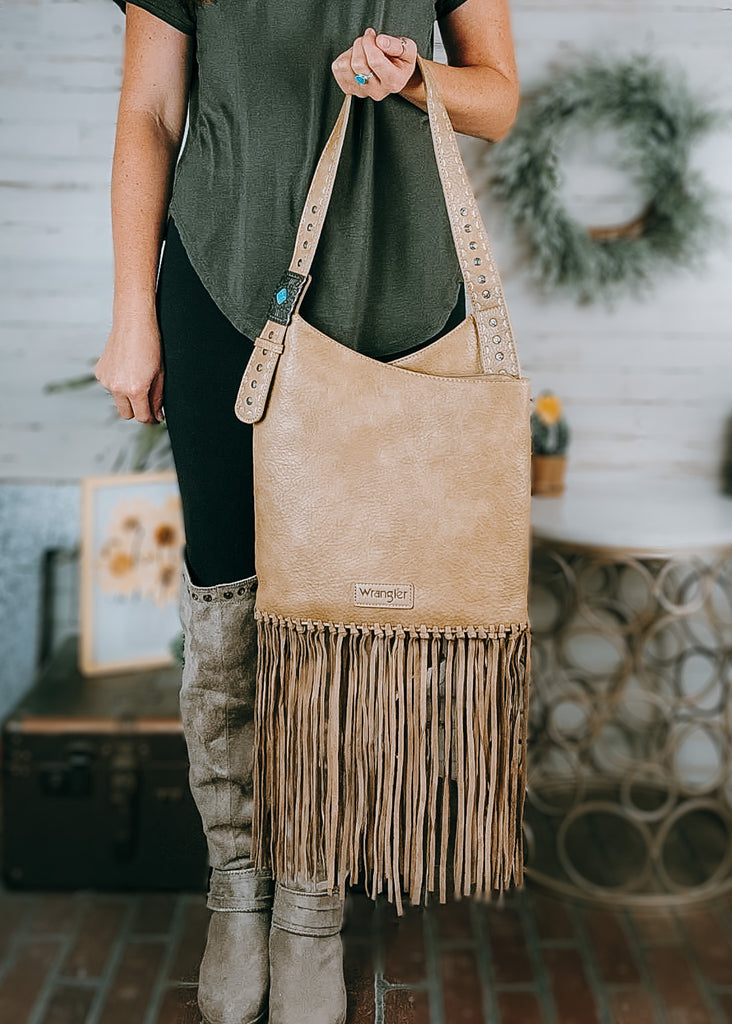 Concealed Carry Tan Turquoise Stone Concho Fringe Hobo, model is wearing an olive green shirt, black leggings and tall tan boots with western decor in the background