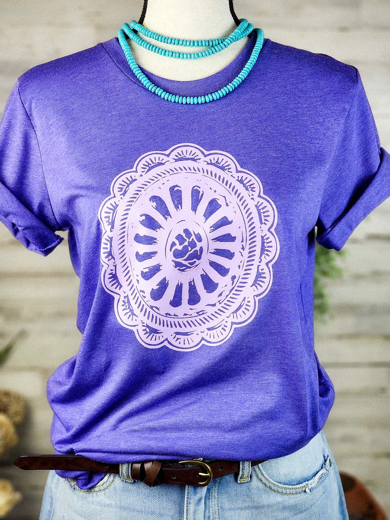 Purple short sleeve tee with lavender print concho design. Shirt hangs from mannequin with turquoise like stone choker necklace. 