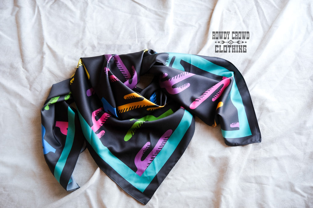 Black wildrag with multi colored cacti prints with teal strip on the borders.  Wild rag is loosely wrapped on white clothe. 