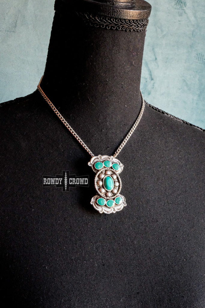 Turquoise like stone necklace with antique silver concho design. Pendant is on a chain and is displayed on a mannequin.