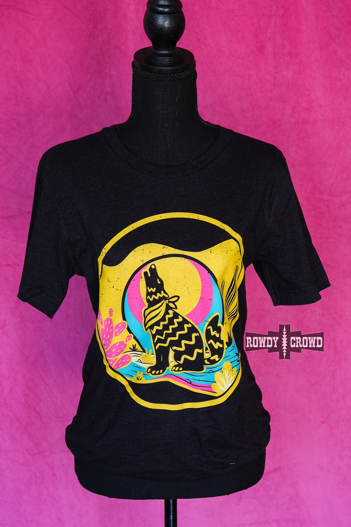 Heather black short sleeve tee with a yellow, blue, and pink desert scene of a coyote howling at the moon. Tee hangs from mannequin. 