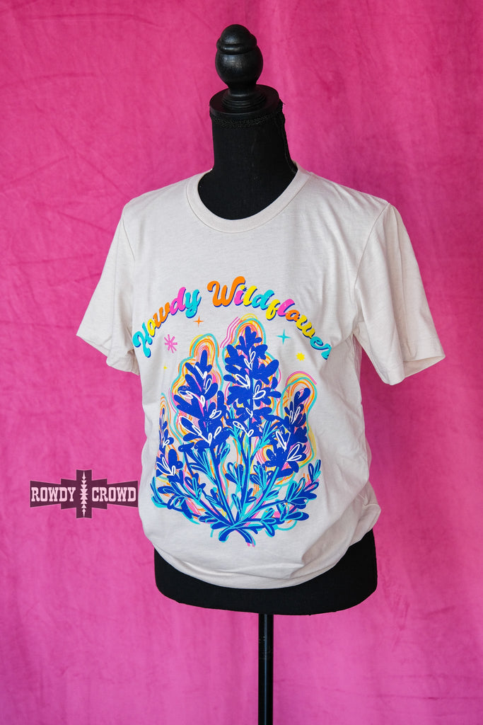 Natural short sleeve with colorful bubble lettering reading "Howdy Wildflower". Wildflower colorful graphic with white heart designs. Tee hangs from mannequin.