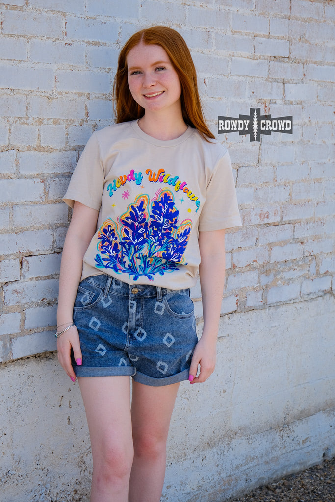 Natural short sleeve with colorful bubble lettering reading "Howdy Wildflower". Wildflower colorful graphic with white heart designs. Model wears this with jean shorts.