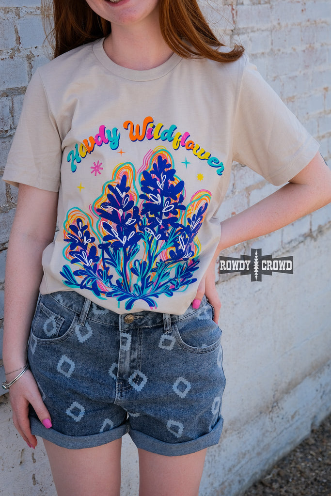 Natural short sleeve with colorful bubble lettering reading "Howdy Wildflower". Wildflower colorful graphic with white heart designs. Model wears this with jean shorts.