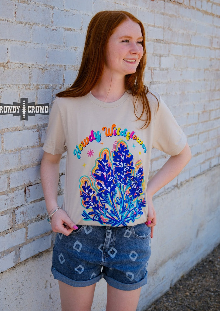 Natural short sleeve with colorful bubble lettering reading "Howdy Wildflower". Wildflower colorful graphic with white heart designs. Model wears this with jean shorts.