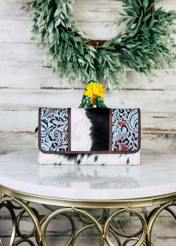 Cowhide wallet with blue embossed floral leather panels on the flap of the wallet. Wallet sits on a marble stool. 
