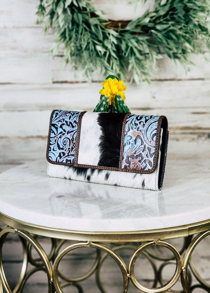 Cowhide wallet with blue embossed floral leather panels on the flap of the wallet. Wallet sits on a marble stool. 