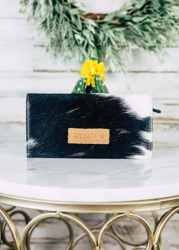 Cowhide snap flap wallet sits on marble table top. Backside of the wallet is shown interior zipper can be seen.