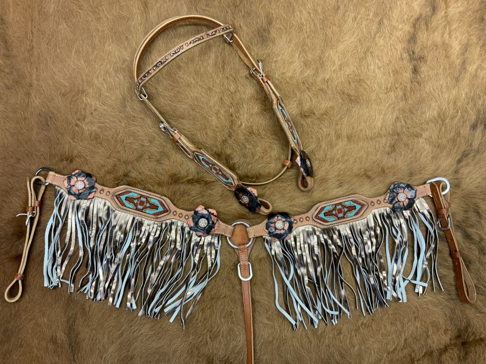 Western light oil headstall set with aztec inlays and gold fringe. Floral conchos decorate the piece with small copper colored small studs. Headstall sets on a cowhide rug.